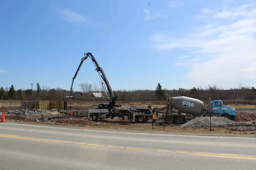 A concrete pump truck delivering fresh ready-mix concrete into formwork for a building foundation