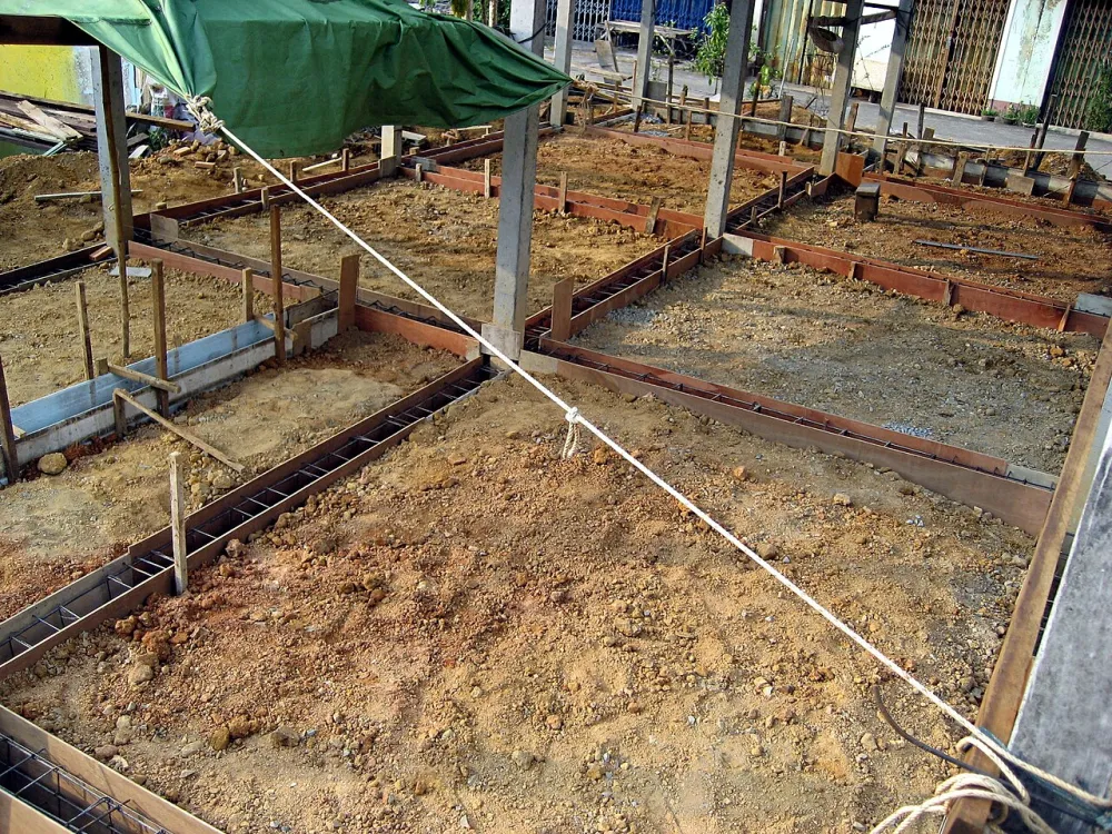 Timber formwork boards set out on bare ground forming a grid of footings, ready for a concrete pour