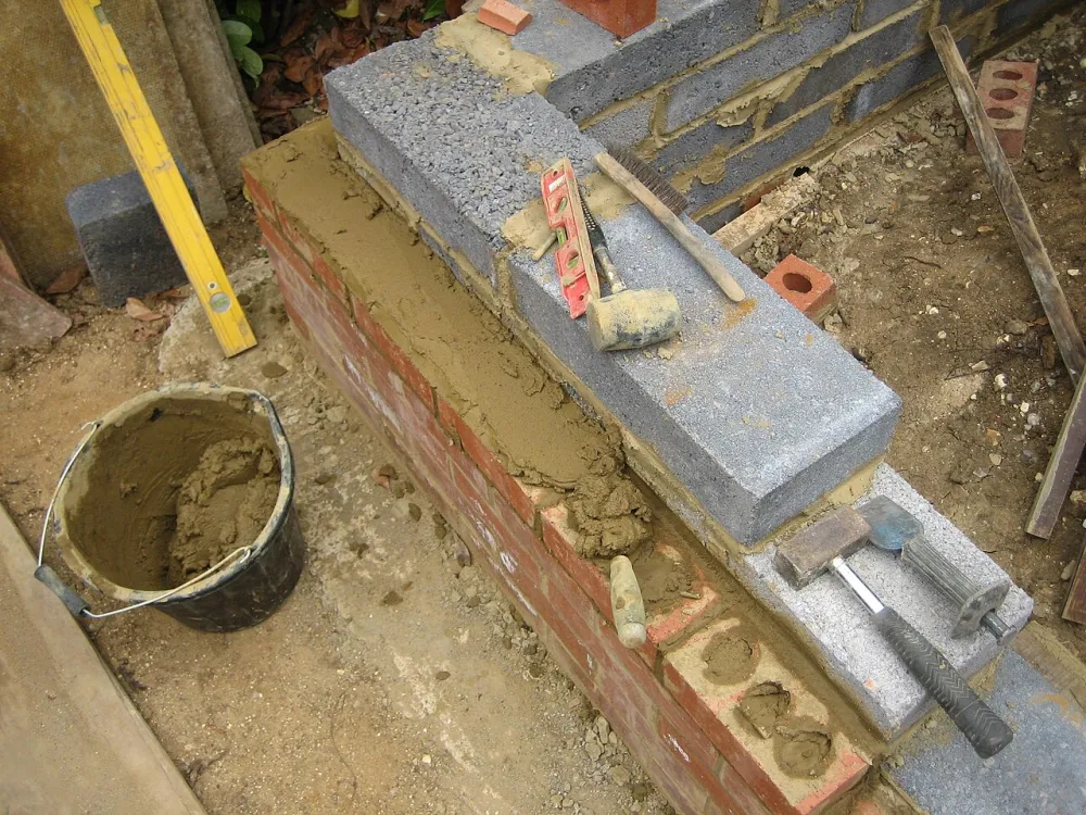 Fresh mortar laid along the top course of a brick and block wall, with a bucket of mixed mortar alongside